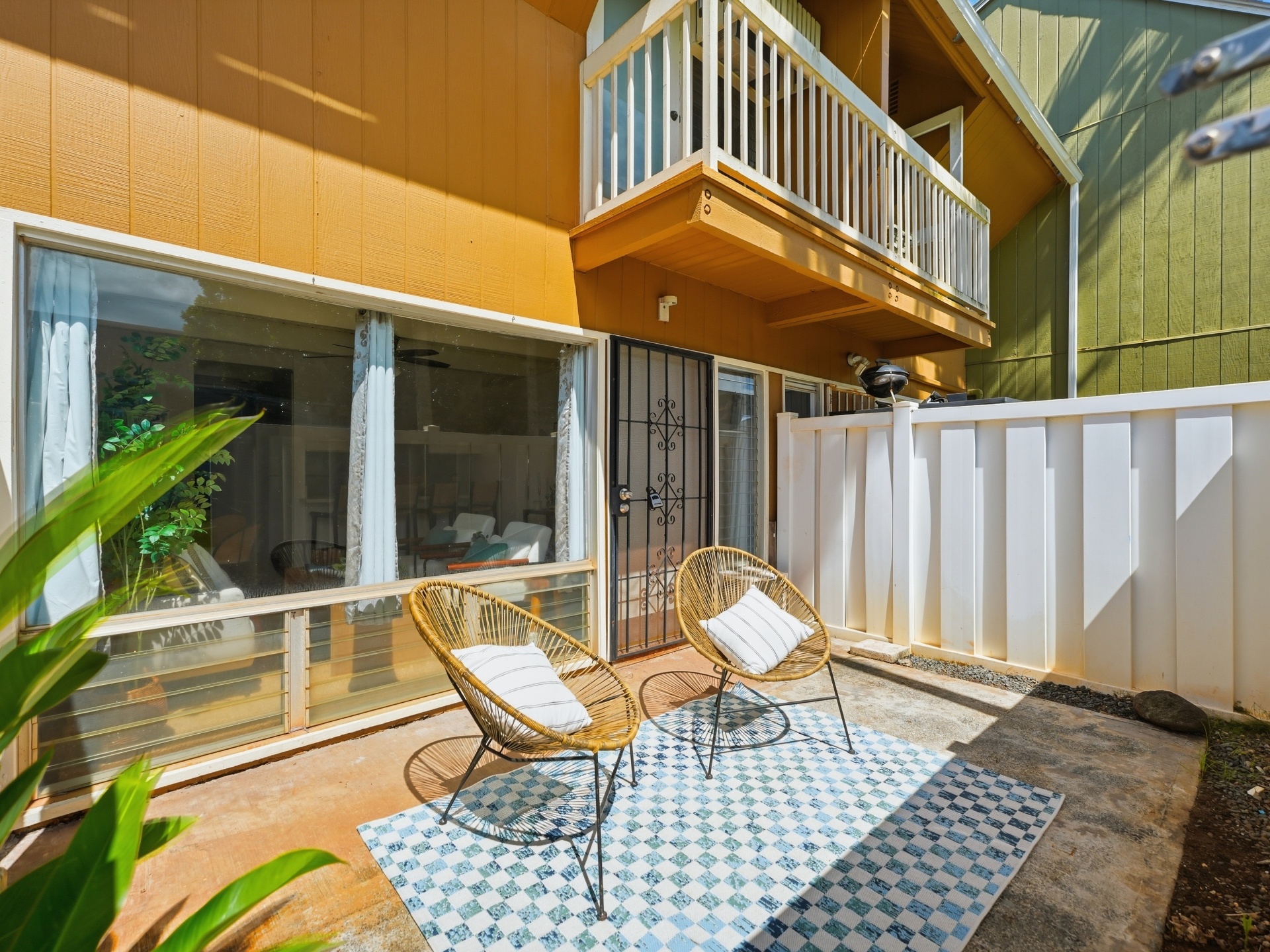 Private fenced courtyard with woven chairs, checkered rug and lush plants